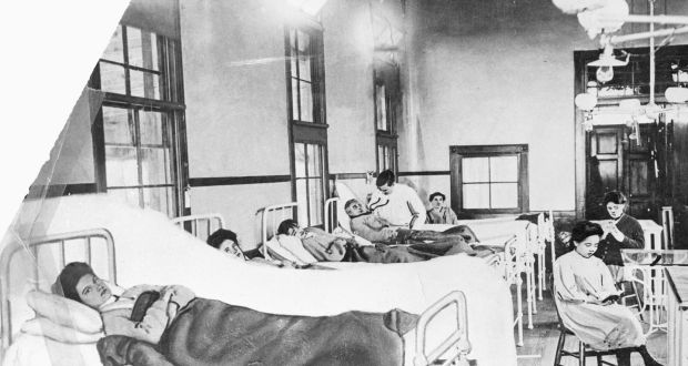a black and white picture of a row of hospital beds. Mary Mallon, a dark-haired woman, is lying in the first bed looking at the camera.