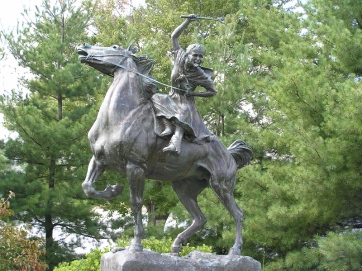 Bronze statue of a woman on a horse sculpted to look like they're in motion. She's holding a wooden stick in her raised hand.